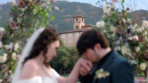 Holly and Beren framed by a floral arch at The Broadmoor with a Colorado mountain backdrop