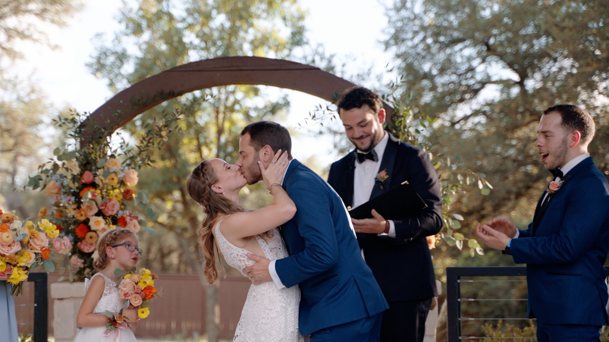 A bride and groom sharing their first kiss under a wooden arch at an outdoor Colorado wedding ceremony, illustrating a key moment in a wedding videography timeline.